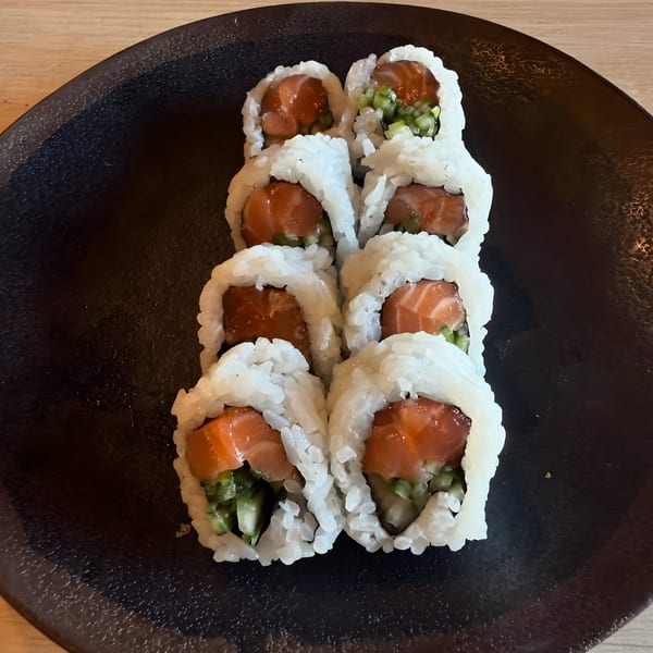 Eight pieces of salmon and cucumber sushi rolls on a dark plate at Sushi Koo.