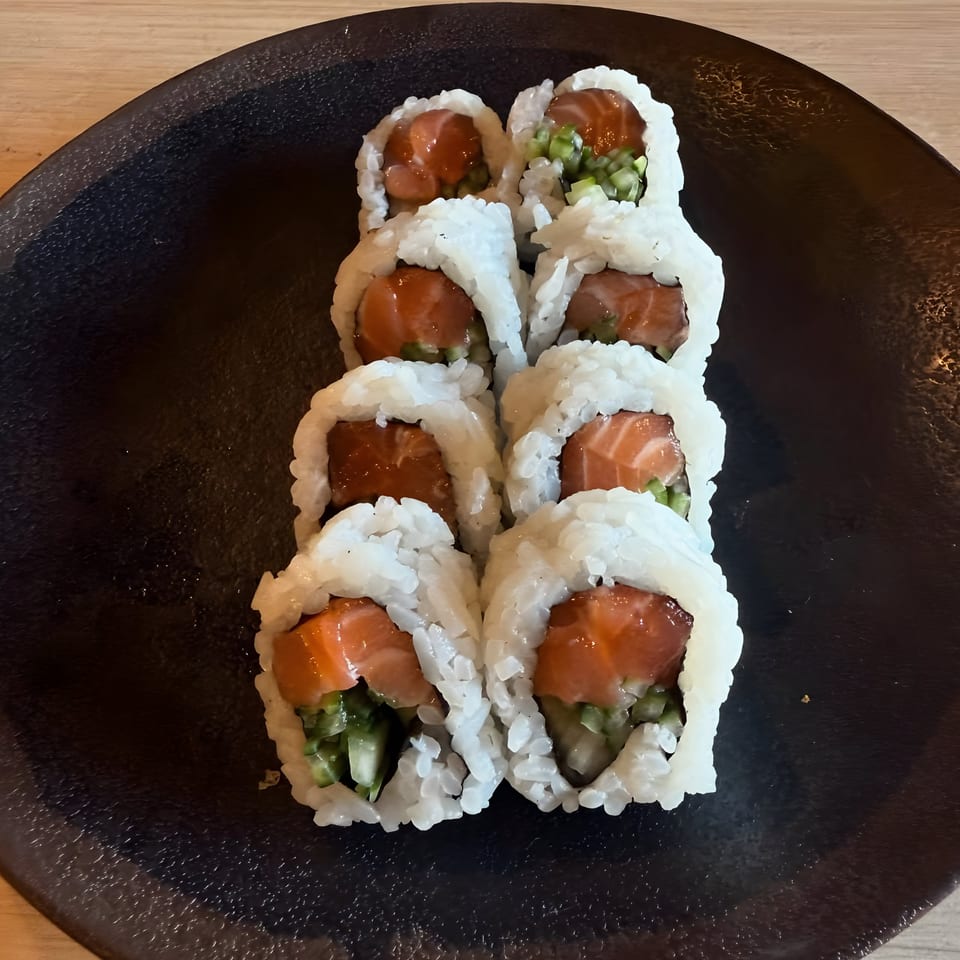 Eight pieces of salmon and cucumber sushi rolls on a dark plate at Sushi Koo.
