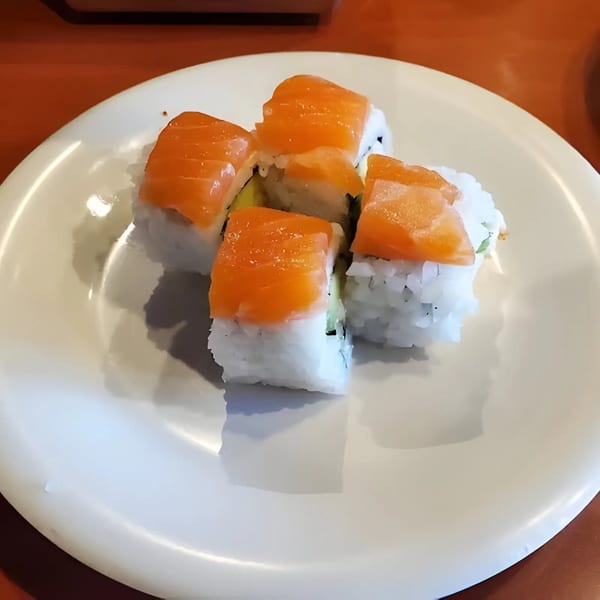 Five salmon sushi rolls with white rice and avocado on a white plate.