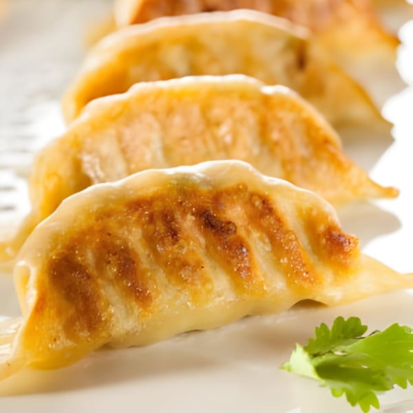 Close-up of golden-brown pan-fried gyoza dumplings, garnished with a sprig of fresh cilantro.