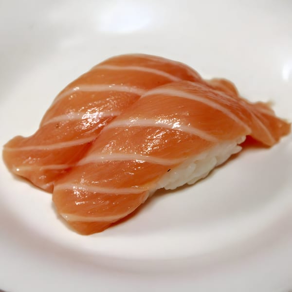 Two pieces of salmon nigiri sushi with glistening orange fish on white rice, on a white plate.