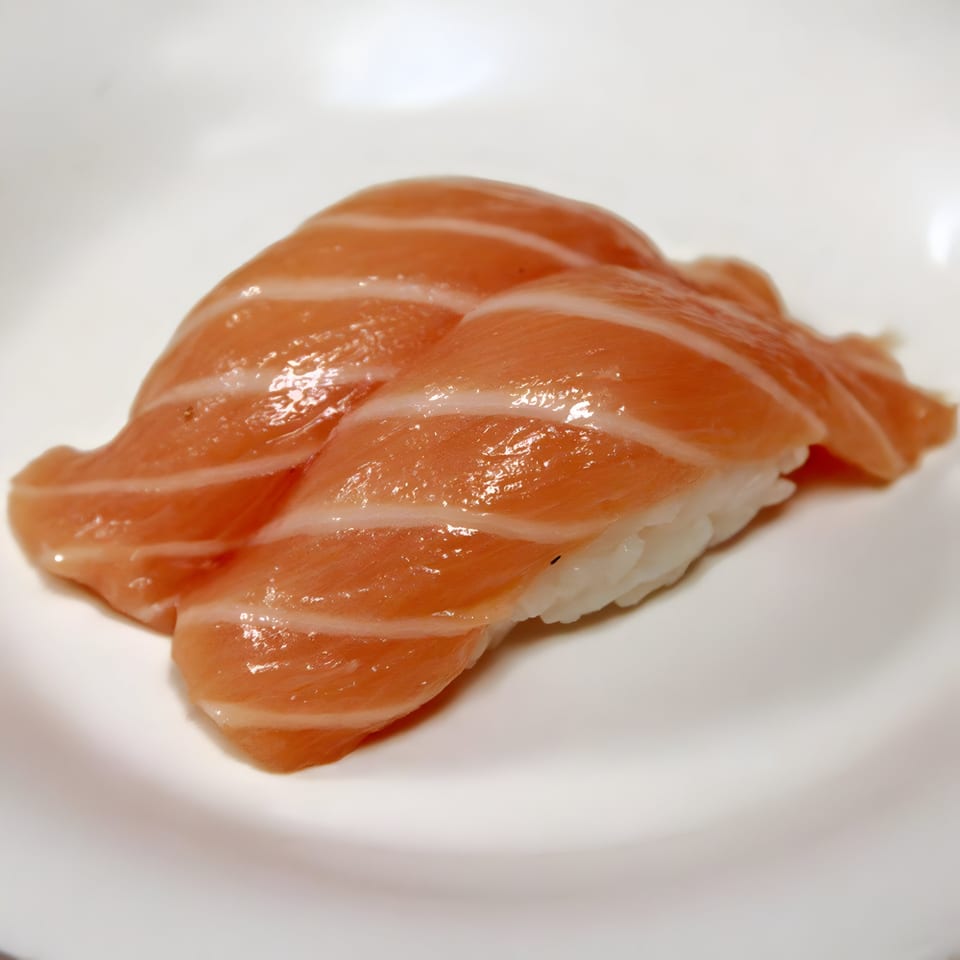 Two pieces of salmon nigiri sushi with glistening orange fish on white rice, on a white plate.