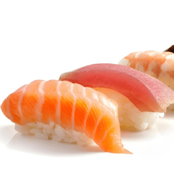 Close-up of three pieces of Sushi Koo nigiri, including salmon, tuna, and shrimp, on a white background.