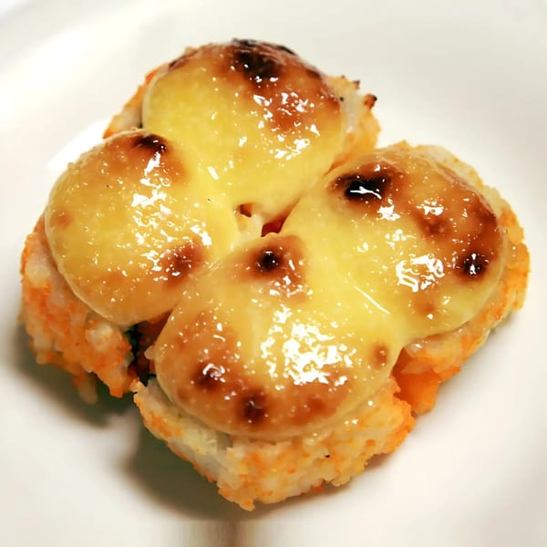 Four pieces of baked sushi with melted, golden-brown cheese on top, on a white plate.